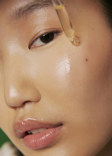 Close-up of a person applying a dropper of serum to their skin.